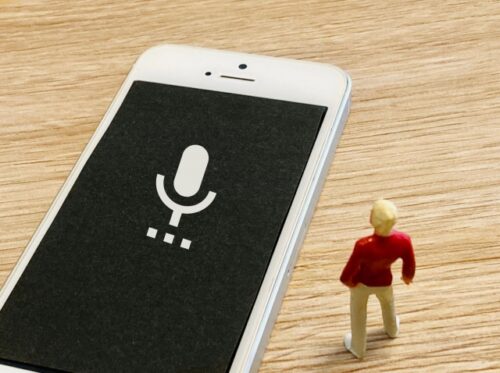 a-smartphone-displaying-a-microphone-icon-on-a-wooden-table-with-a-miniature-figure-standing-next-to-it-representing-practical-voice-and-ai-english-apps