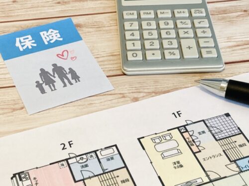 A calculator, a pen, and a house floor plan with a card showing a family illustration and the word insurance, representing group credit life insurance for mortgages.
