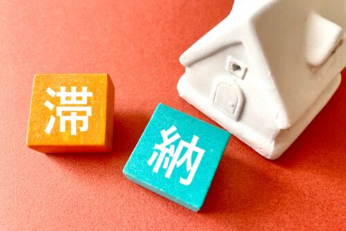 A white house model with wooden blocks displaying the Japanese characters for late payment, representing the impact of credit delinquency on mortgage screening