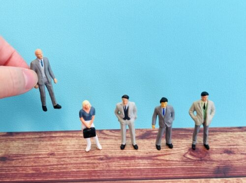 A hand picking up one figurine from a group of people in various business attire, representing the evaluation of occupation and employment status in mortgage screening