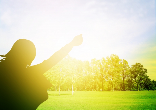 silhouette-of-a-person-raising-their-arm-towards-the-sunlight-on-a-grassy-field