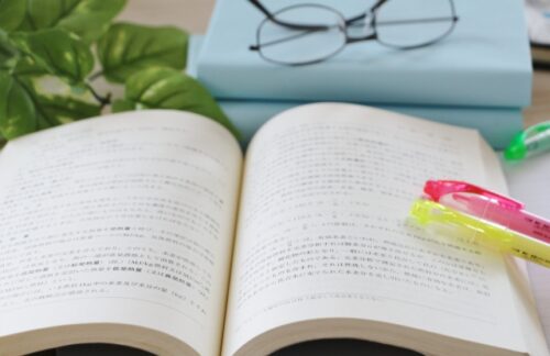 an-open-textbook-with-colorful-highlighters-glasses-and-stacked-books-on-a-desk-representing-recommended-reading-materials-for-english-study