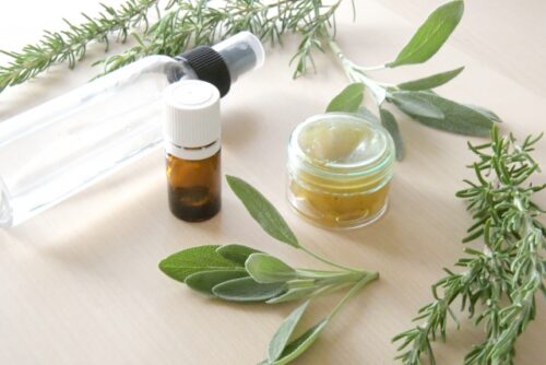 n-essential-oil-bottle-spray-bottle-and-small-jar-surrounded-by-fresh-rosemary-and-sage-leaves-on-a-wooden-table
