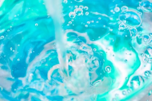 close-up-of-clear-water-pouring-and-splashing-with-bubbles-in-light-blue-liquid